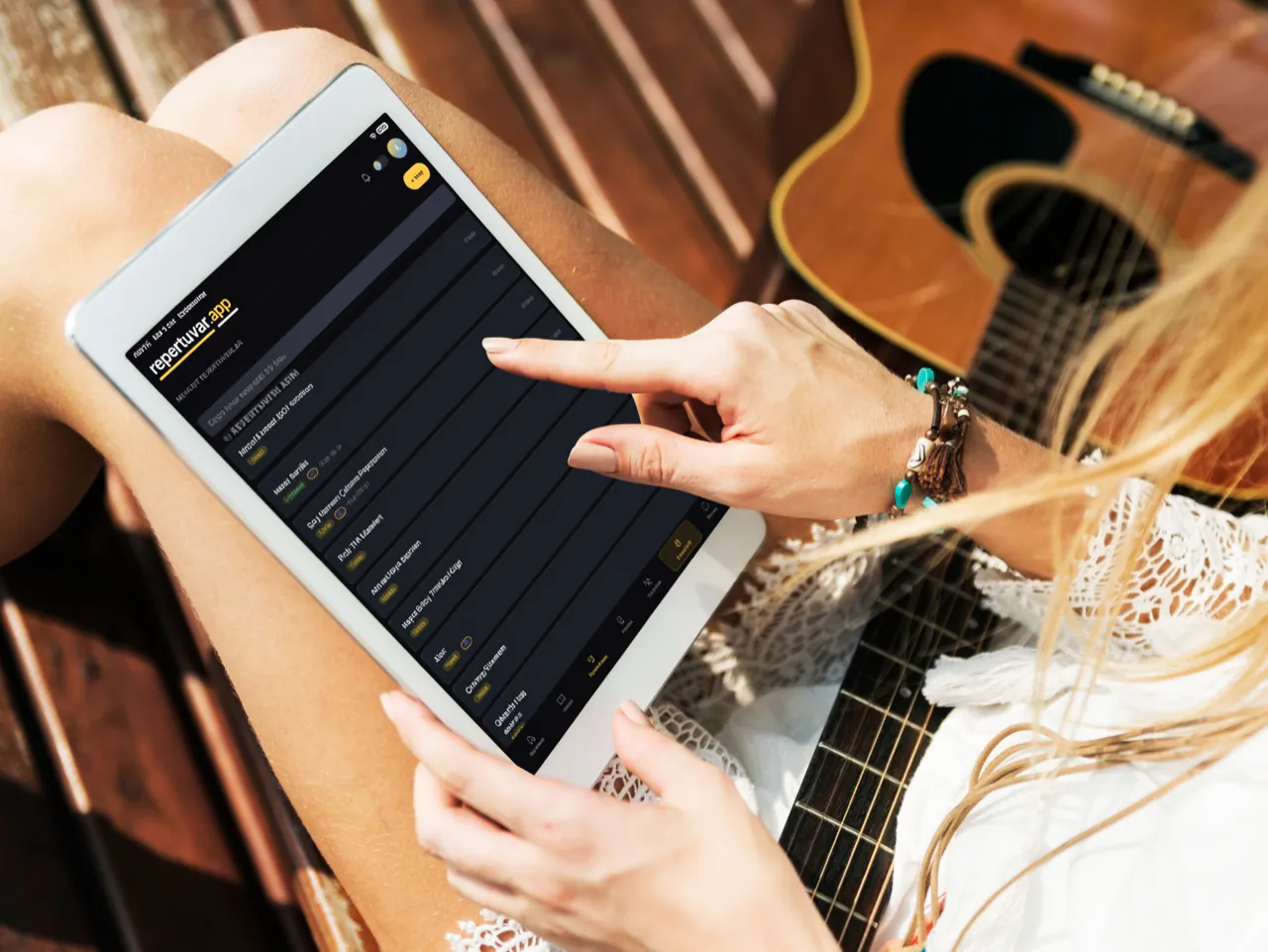Gitarı yanında, tablette Repertuvar.app listesinden eser seçen müzisyen